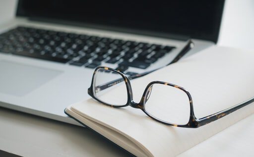 glasses and a notebook beside a laptop